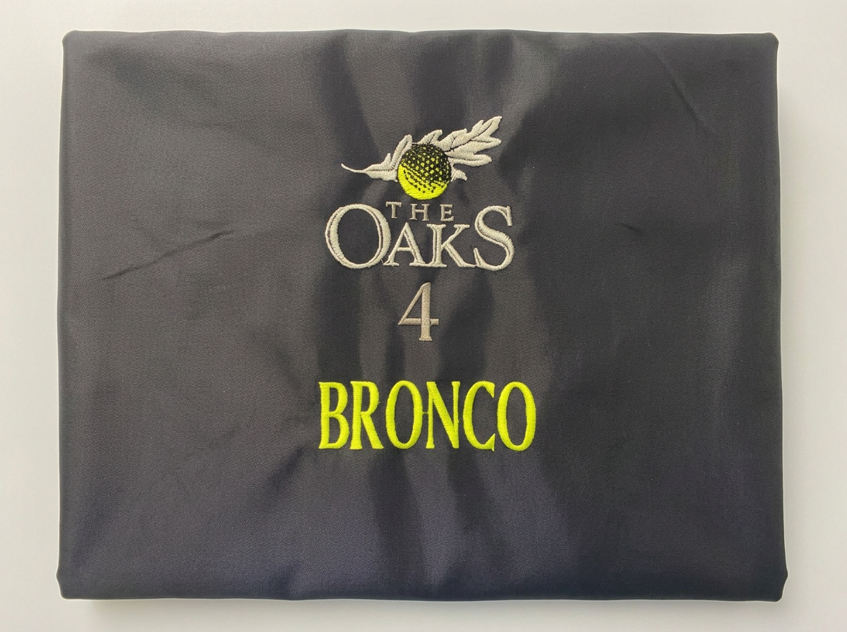Dark jacket with The Oaks 4 Bronco embroidered design in cream and neon yellow thread.